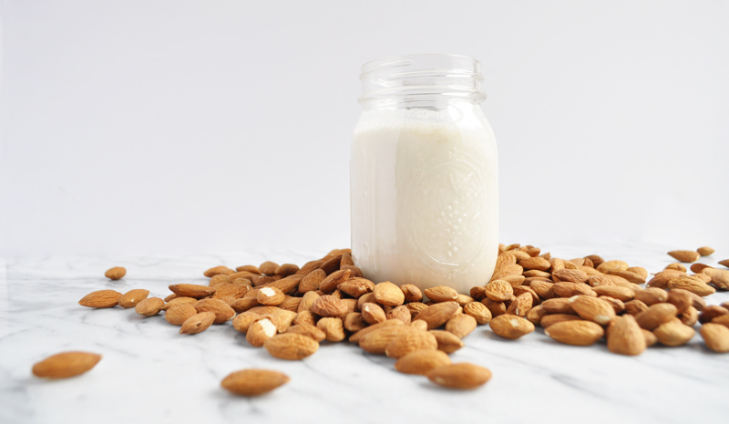 Image of a jar of nut milk surrounded by almonds on a marble countertop