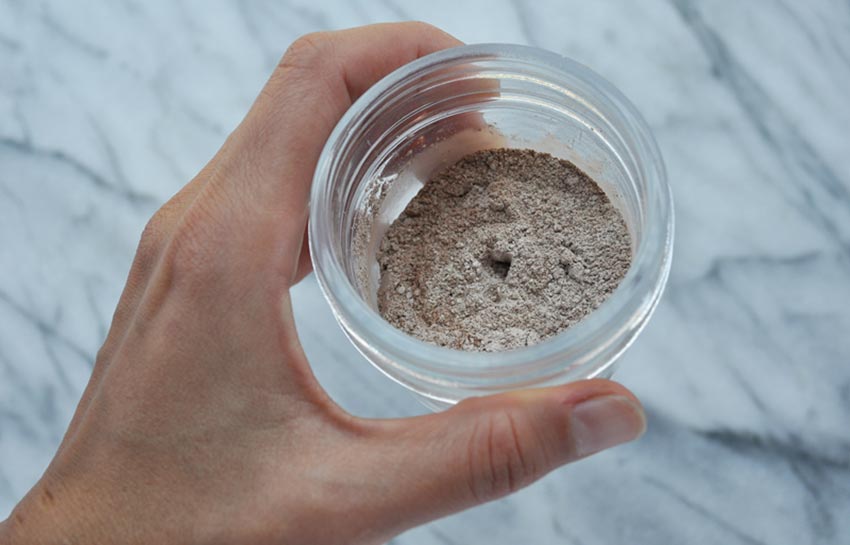 Image of a hand holding a glass jar of bentonite clay tooth powder