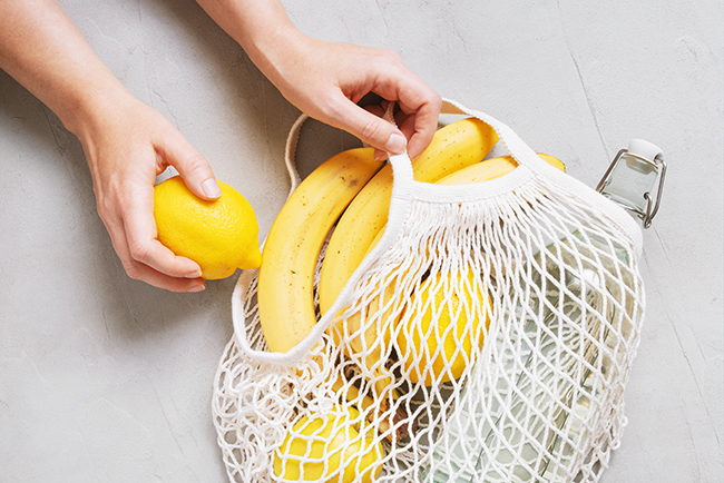 Image of a hand holding the mesh bag with fresh lemons and bananas - switching to greener alternatives is one of the best sustainable new year resolutions you can make
