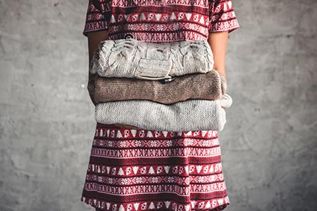 Image of a woman holding a stack of knitted sweaters