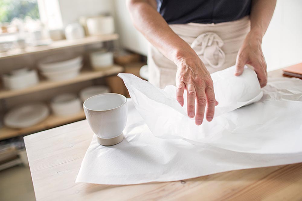 Image of a person wrapping a piece of pottery in tissue paper