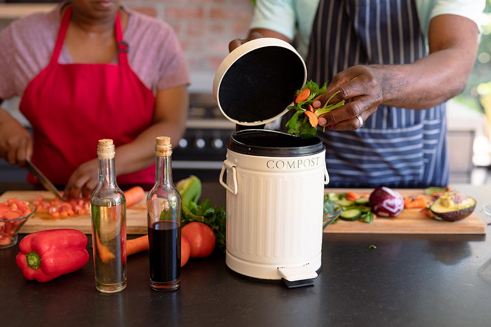 Image of two people putting food scraps into a kitchen compost bin as they cook 